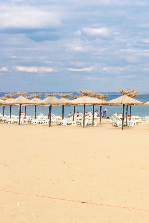 Plage des Sables d'Or en Bulgarie avec rangées de parasols en paille et chaises longues face à la mer Noire.