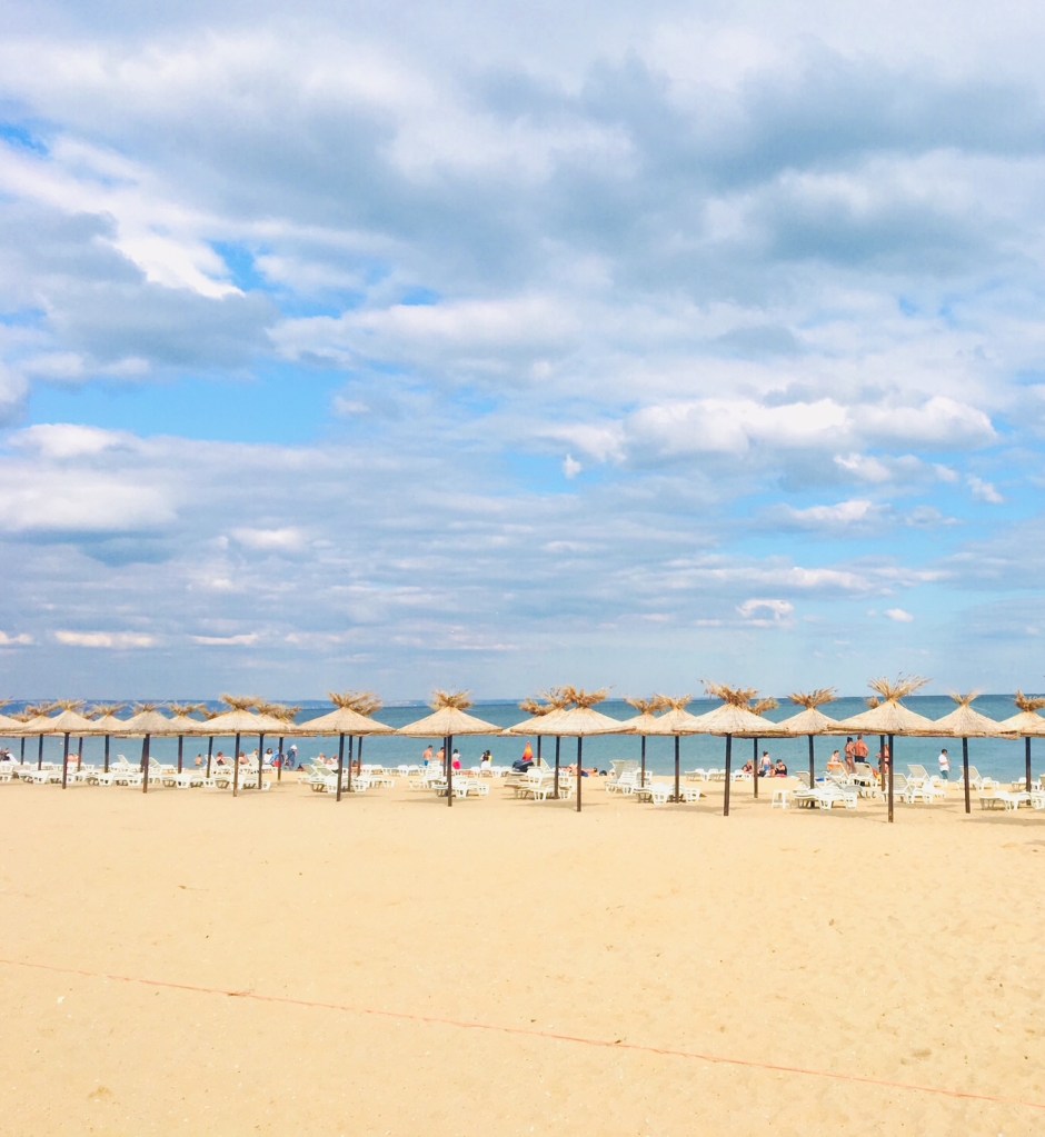 Empty beach at Golden Sands, Bulgaria, with folded umbrellas and the Black Sea shimmering under a dramatic summer 