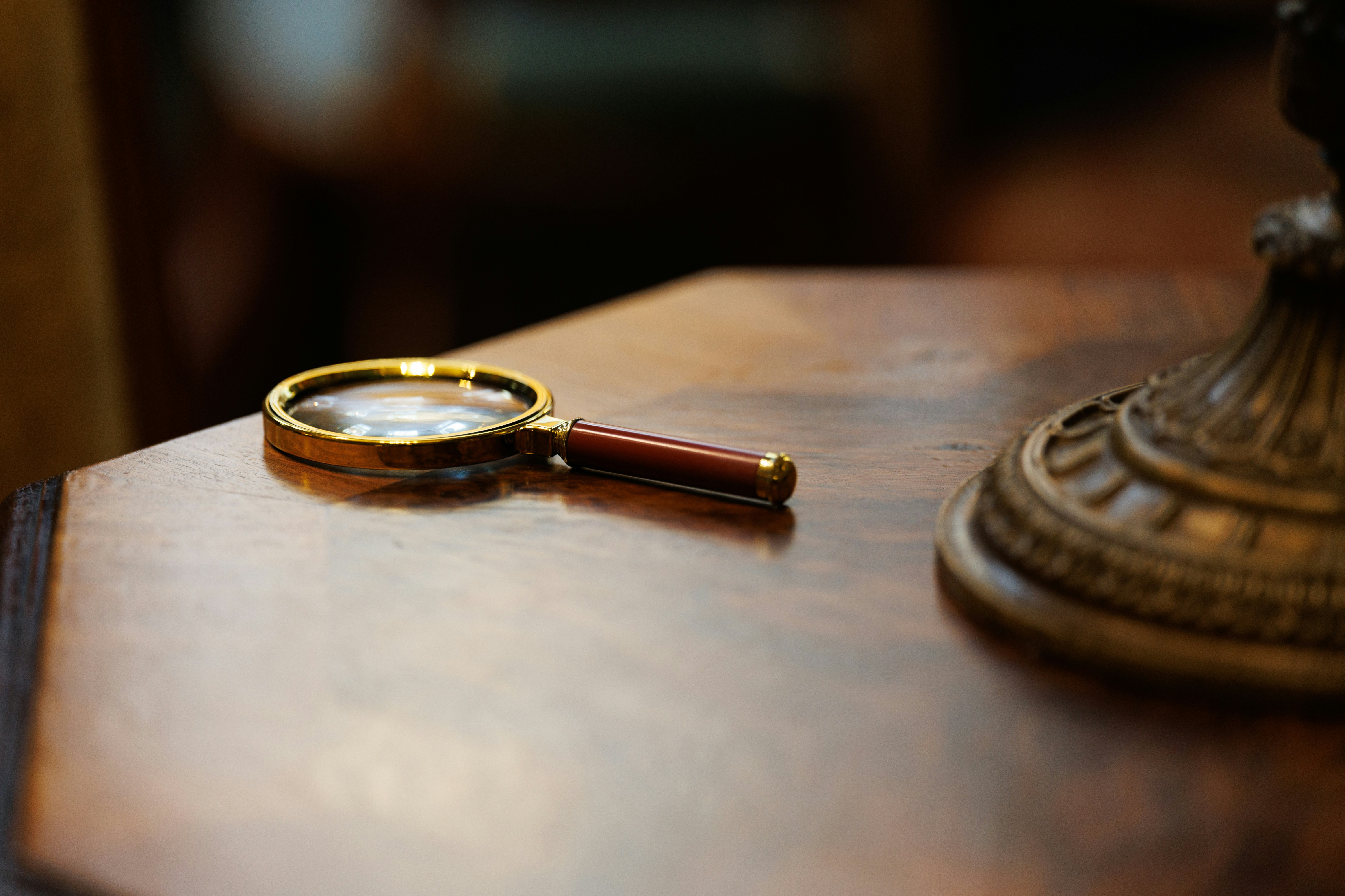 A brass magnifying glass resting on a wooden table, next to an ornate bronze object - an invitation to look more closely.