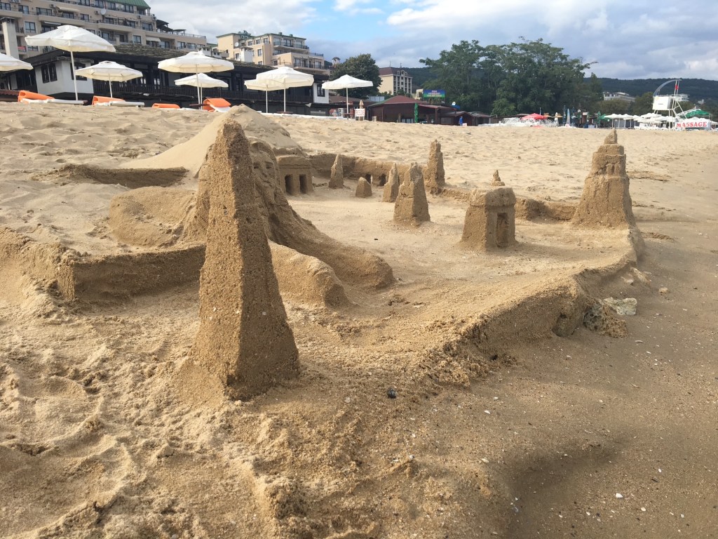 Château de sable élaboré sur la plage des Sables d'Or en Bulgarie, avec hôtels et parasols en arrière-plan.