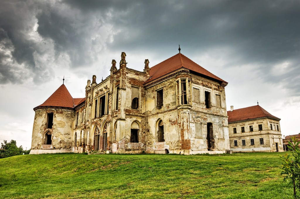 The ruined facade of Bánffy Castle in Bonțida, Transylvania, under a stormy sky.